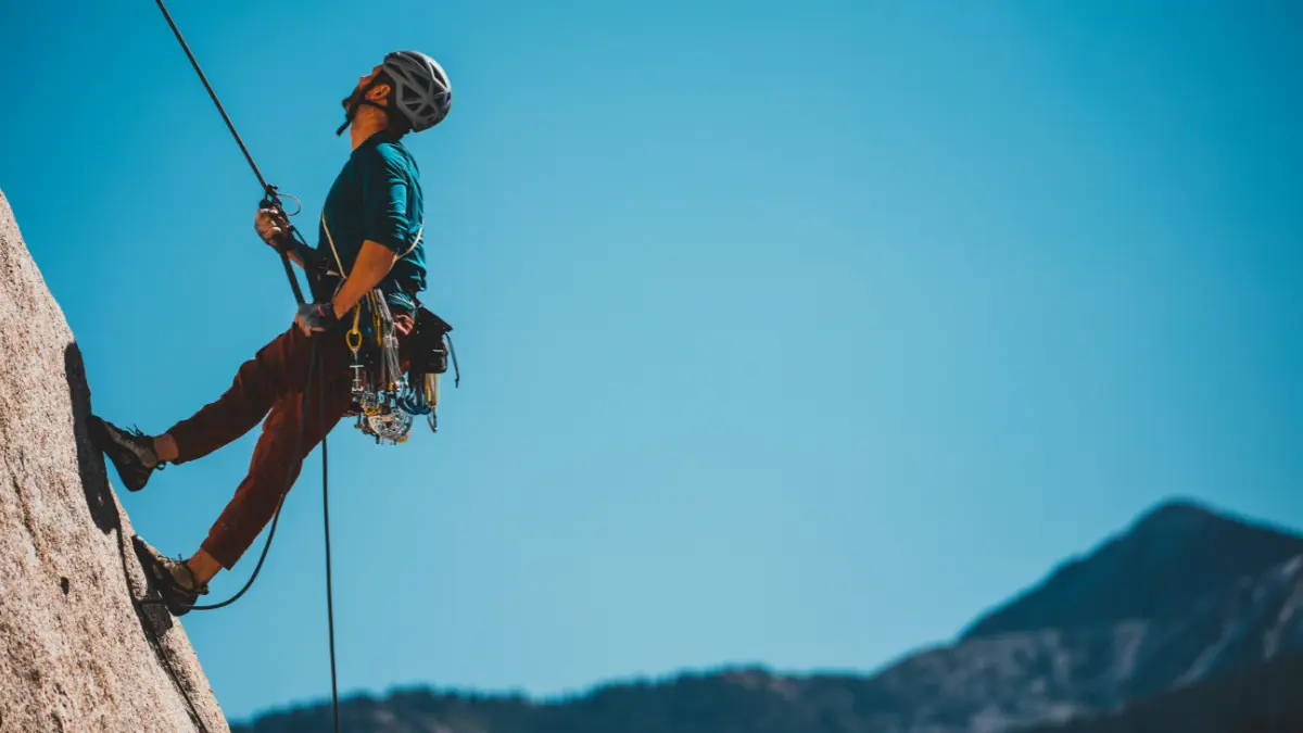 Uomo che arrampica su una parete di roccia con attrezzatura da alpinismo da cintura sotto un cielo azzurro.