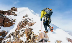 Alpinista equipaggiato durante un'ascensione su una montagna innevata in alta quota.