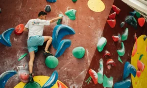 Persona che pratica bouldering arrampicandosi su una parete artificiale indoor senza imbracatura.