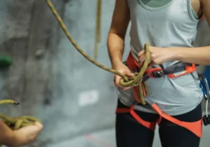 Primo piano di una donna che sta facendo un nodo con la corda sulla sua imbragatura da arrampicata.